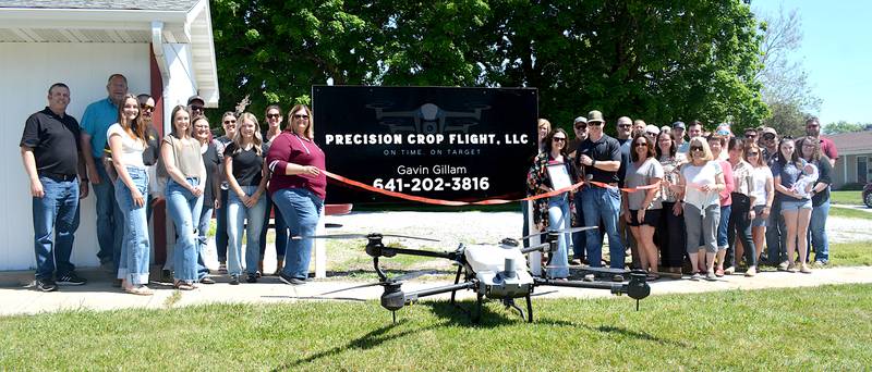 Members of the Chamber of Commerce pose outside the new Precision Crop Flight sign during the ribbon-cutting ceremony. The company's drone sits on the grass in front of the ribbon, which is bing cut by Gavin Gillam.